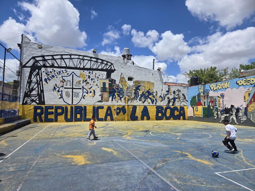 campo da calcio con bambini che giocano e murale Republica de La Boca sulla sfondo